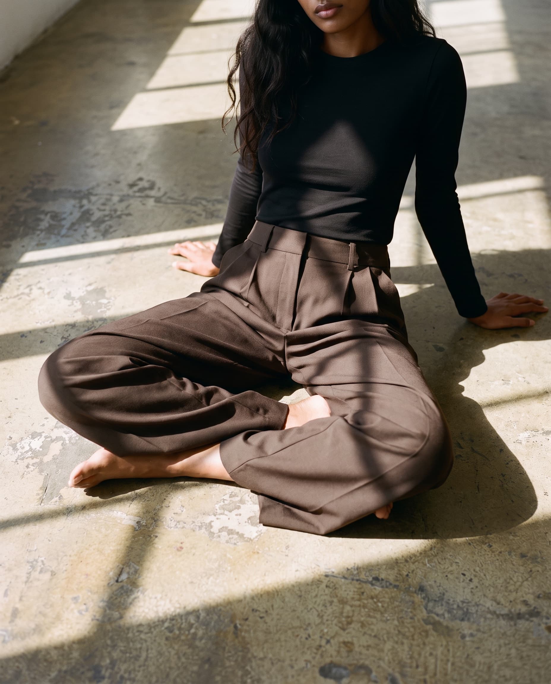 Brown pleated trousers, model seated on a sunlit loft floor